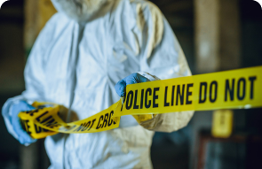 Person in protective suit and gloves holding yellow police line tape at a crime scene.
