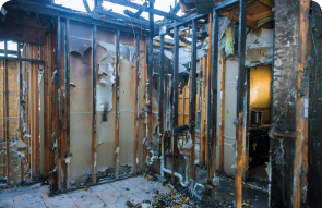 Room with charred and exposed wall studs, damaged insulation, and debris on the floor, showing severe fire damage throughout the interior.